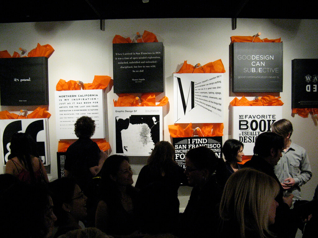 People looking at wall display of black and white shopping bags with orange tissue paper