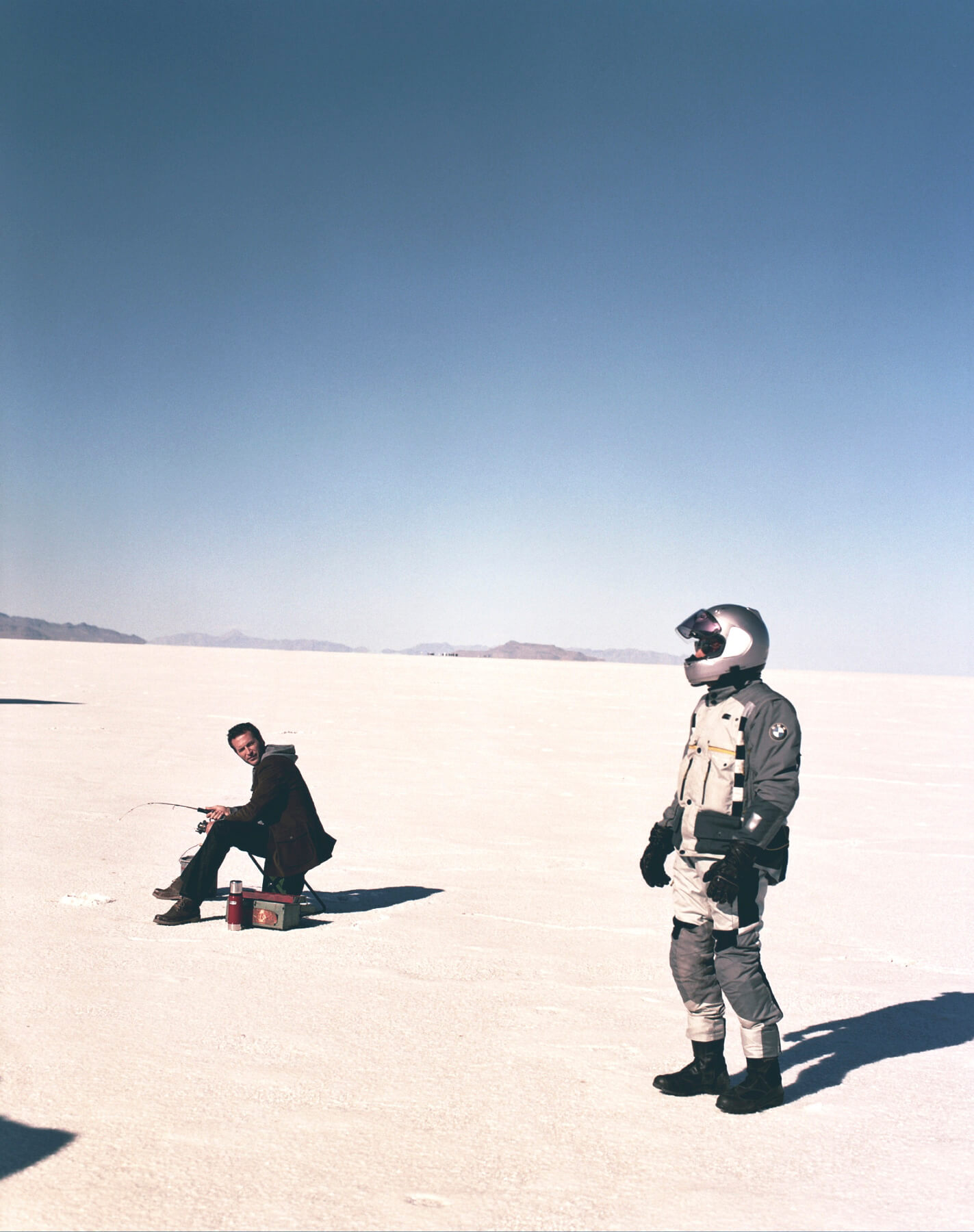 Man fishing while looking at someone wearing silver motorcycle helmet