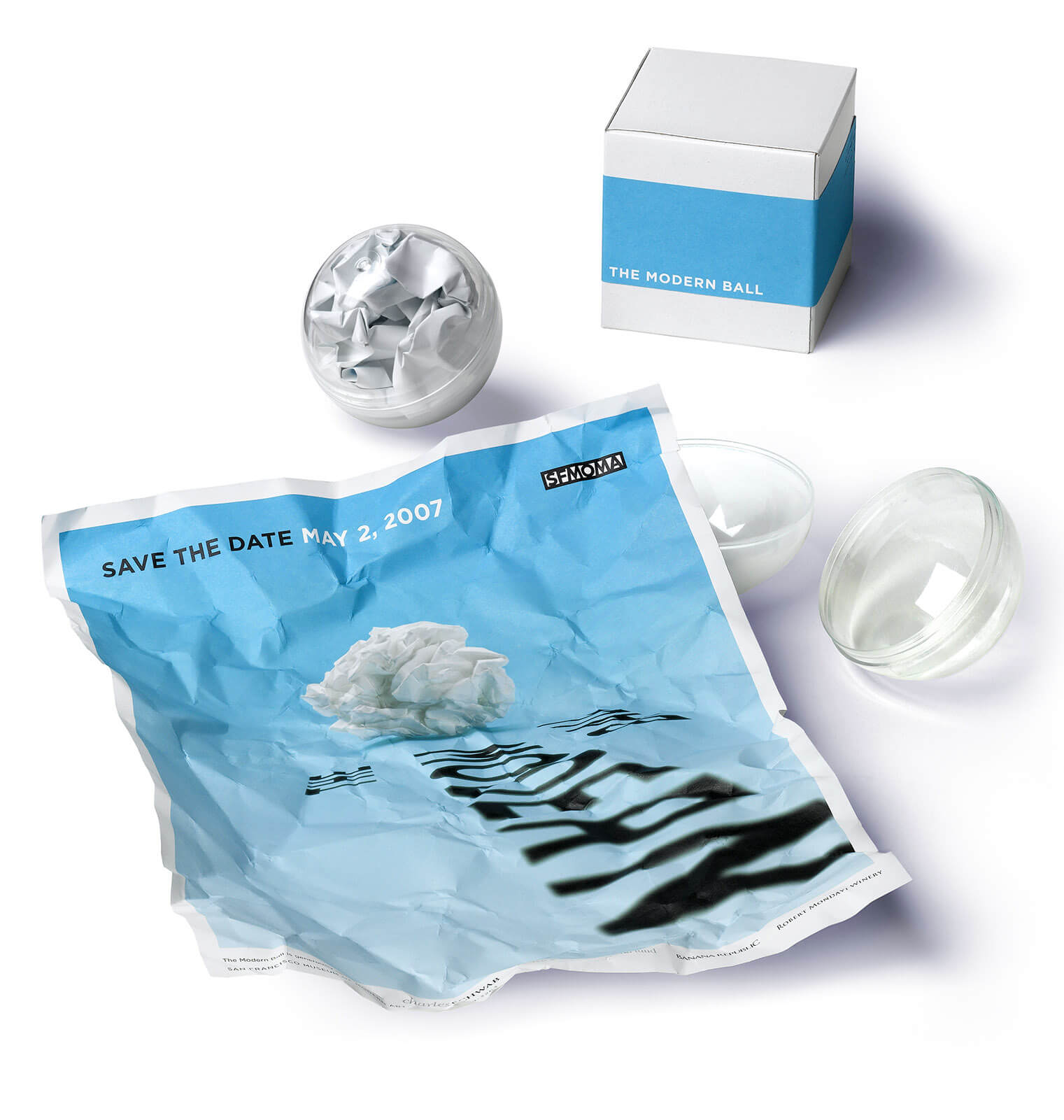 White box with blue band behind a clear plastic sphere containing crumpled paper and an un-crumpled piece of paper with light blue artwork
