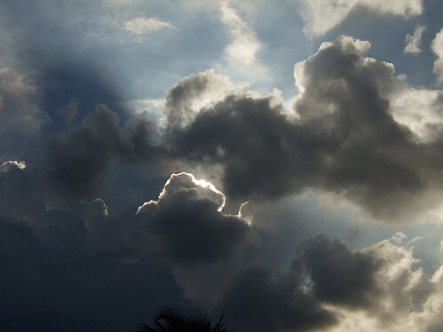 Light peering out from behind clouds in partially dark sky