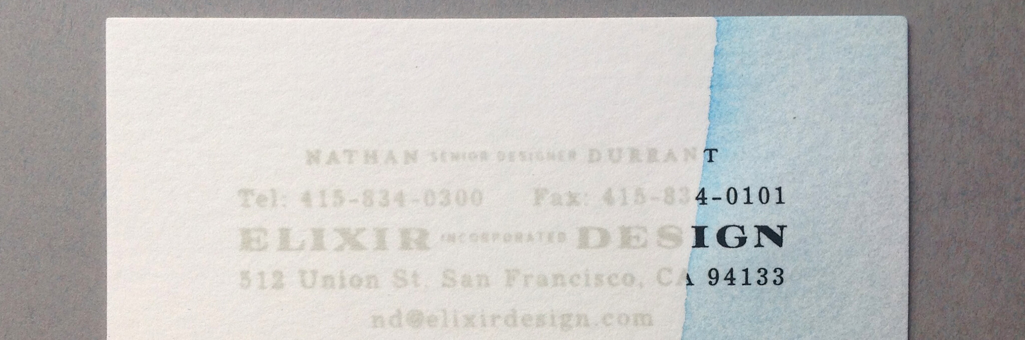 White business card partially dipped in light blue ink on right side