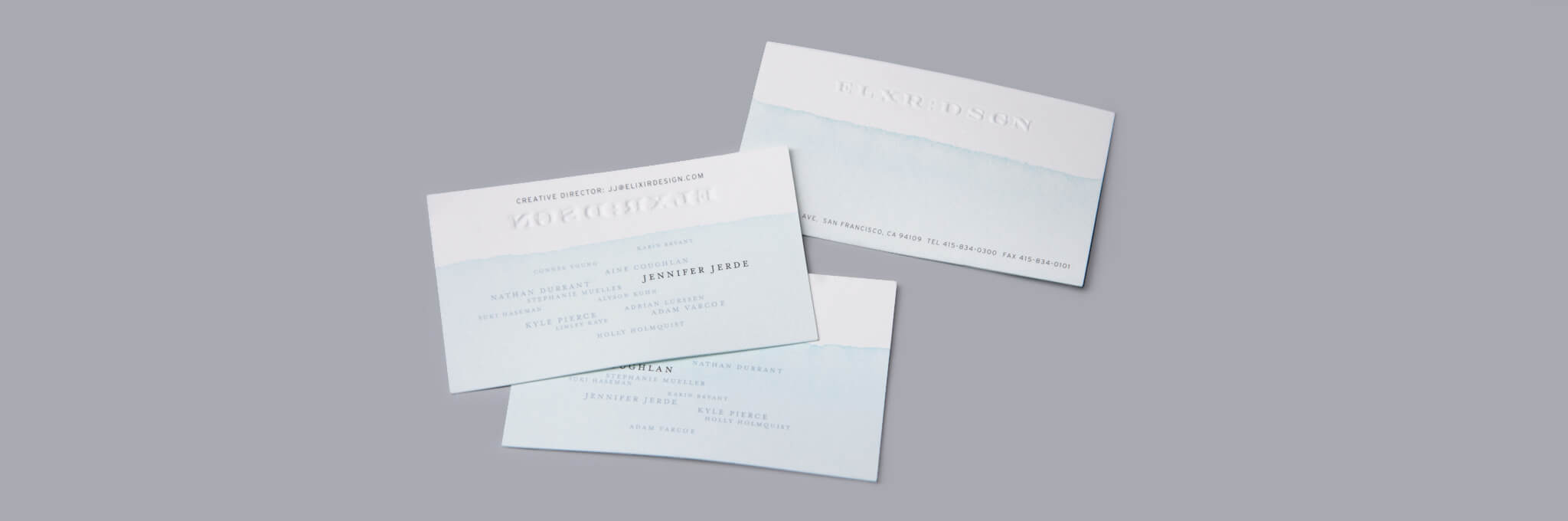 3 white business cards partially dipped in light blue ink on gray background