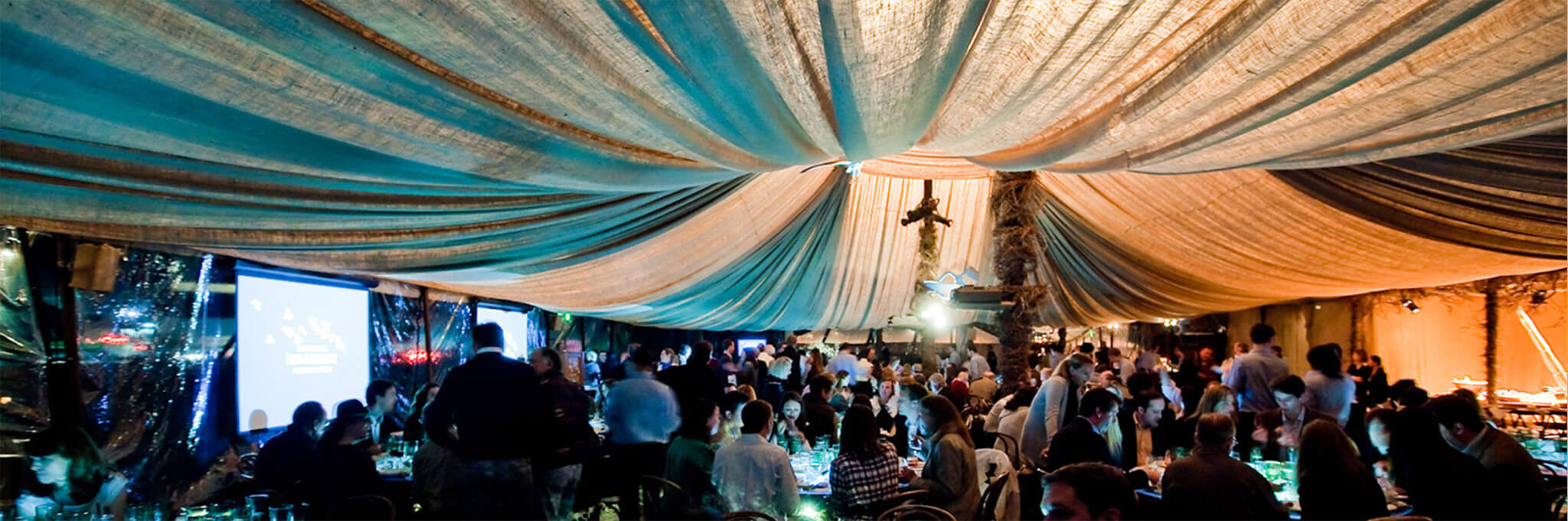 Blue and white draped ceiling above crowds of guests at dinner tables