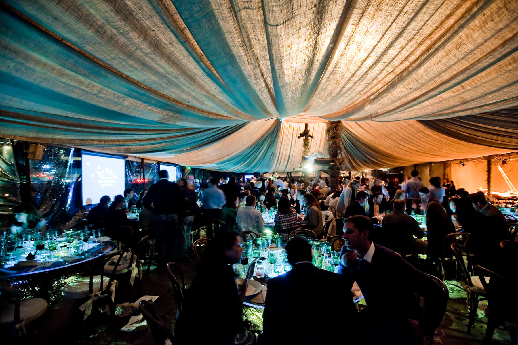 Blue and white draped ceiling above crowds of guests at dinner tables