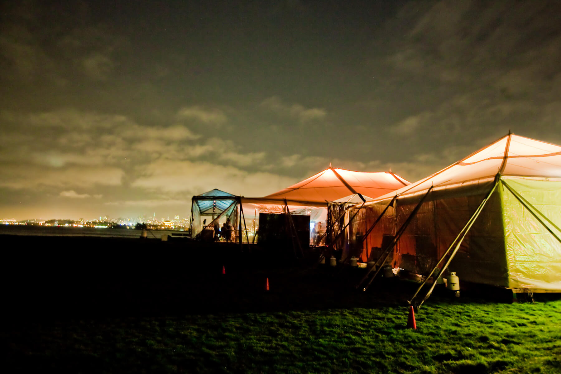 3 blue and orange lit tents in field at night