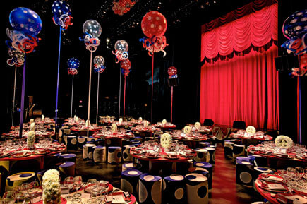 Gala room with red, white, blue table decor, balloons, and red curtain