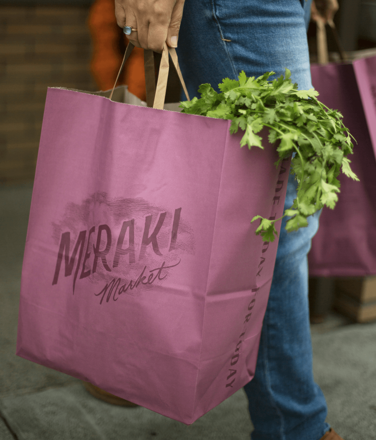 Person carrying pink Meraki cloud logo grocery bag with greens peeking out